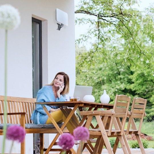 Woman sitting outside of her home at a wood table talking on the phone in front of a laptop